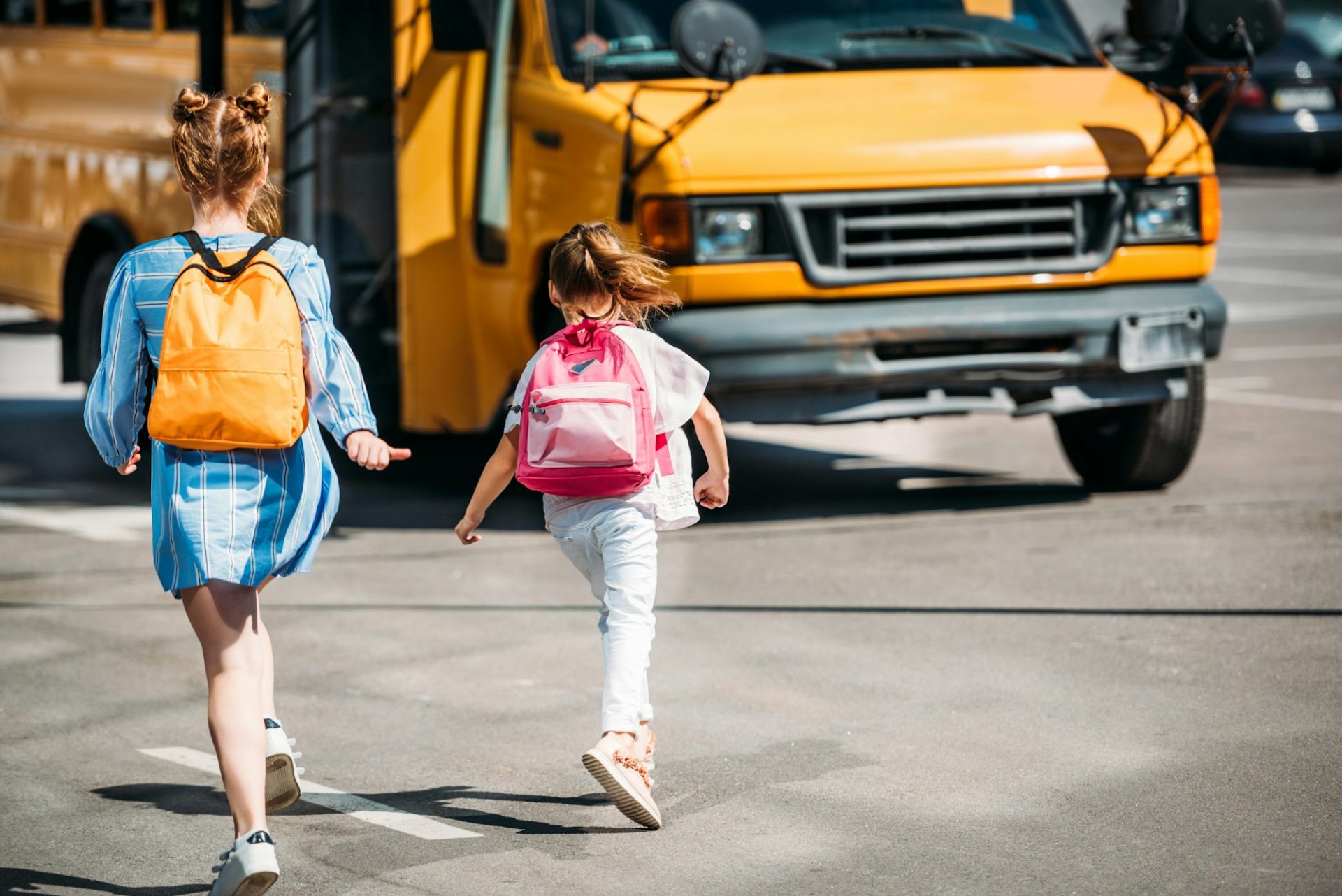 rear-view-of-schoolgirls-with-backpacks-running-to-school-bus